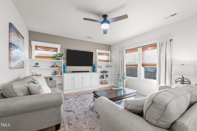 living area featuring light wood-style floors, visible vents, and ceiling fan