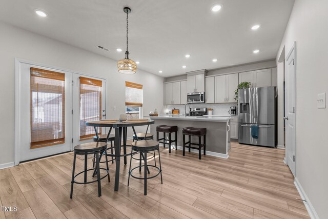 kitchen with stainless steel appliances, light countertops, hanging light fixtures, backsplash, and light wood-style flooring