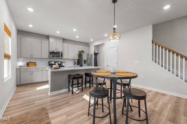 kitchen featuring an island with sink, appliances with stainless steel finishes, decorative light fixtures, gray cabinets, and light countertops