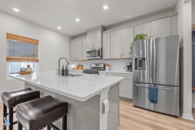 kitchen featuring a sink, a kitchen island with sink, stainless steel appliances, and light countertops