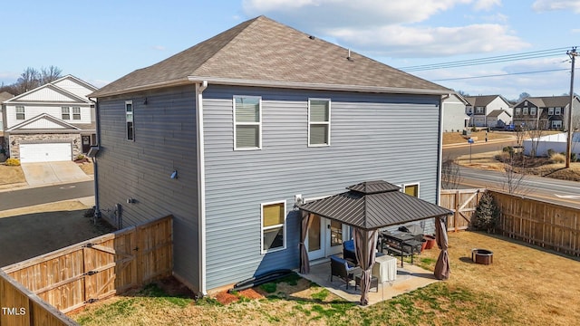 rear view of property featuring a fenced backyard, a residential view, roof with shingles, a gazebo, and a patio area