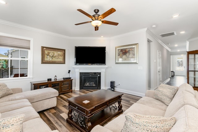 living room with baseboards, visible vents, a glass covered fireplace, ornamental molding, and dark wood-type flooring