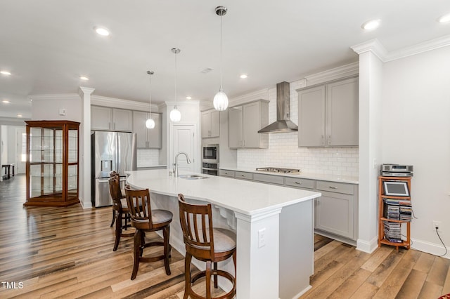 kitchen with decorative light fixtures, stainless steel appliances, light countertops, wall chimney exhaust hood, and a center island with sink