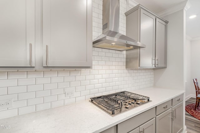 kitchen with light stone countertops, stainless steel gas stovetop, decorative backsplash, wall chimney exhaust hood, and crown molding