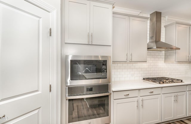 kitchen featuring stainless steel appliances, light countertops, backsplash, and wall chimney exhaust hood