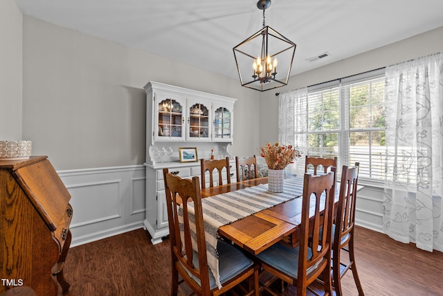 dining space featuring a chandelier, dark wood-type flooring, and a wainscoted wall