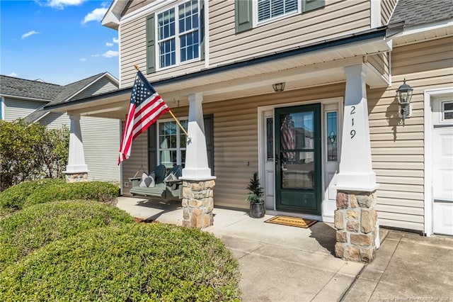 entrance to property featuring a porch and a shingled roof