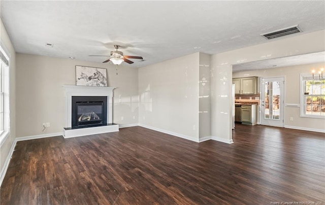 unfurnished living room featuring a glass covered fireplace, visible vents, dark wood finished floors, and baseboards