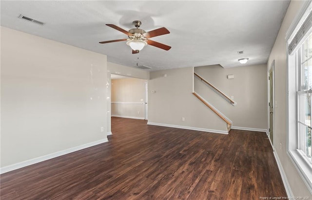 unfurnished room featuring dark wood-style flooring, visible vents, a ceiling fan, baseboards, and stairs