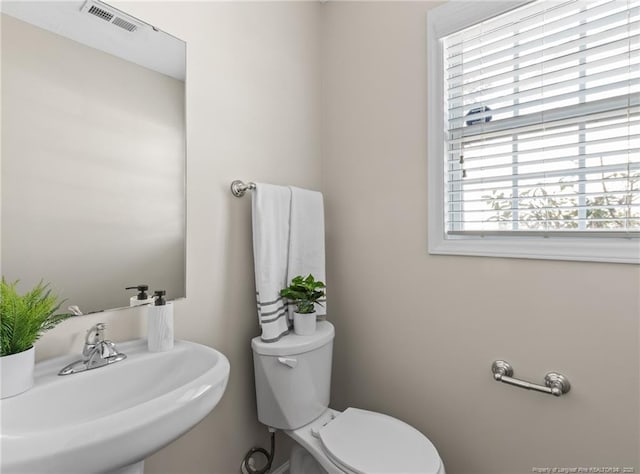 half bath featuring toilet, a sink, and visible vents