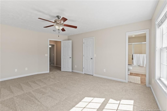 unfurnished bedroom featuring light colored carpet, connected bathroom, baseboards, and ceiling fan