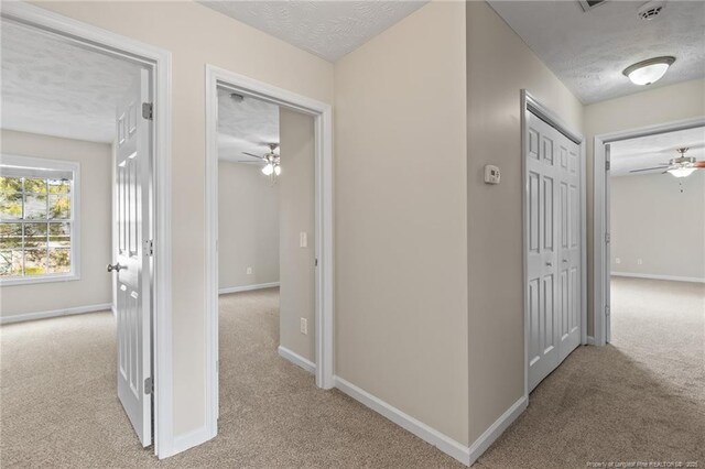 corridor with baseboards, a textured ceiling, and light colored carpet