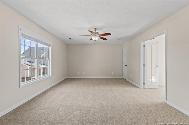 empty room with a ceiling fan, light colored carpet, and baseboards