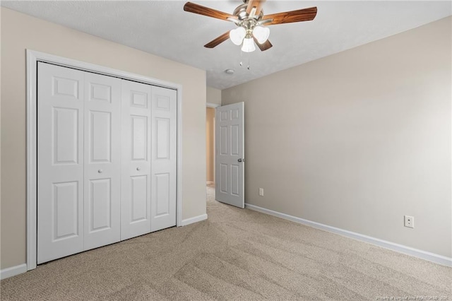 unfurnished bedroom with light carpet, a closet, a ceiling fan, and baseboards