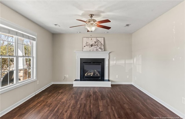unfurnished living room with ceiling fan, a glass covered fireplace, visible vents, baseboards, and wood finished floors