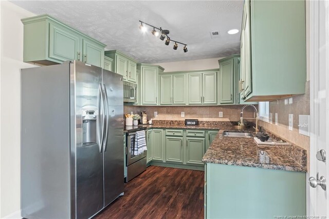 kitchen featuring tasteful backsplash, appliances with stainless steel finishes, green cabinets, a sink, and dark wood-type flooring
