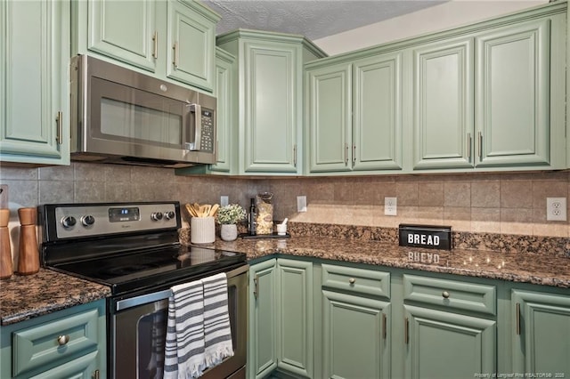 kitchen featuring green cabinetry, dark stone countertops, appliances with stainless steel finishes, and tasteful backsplash