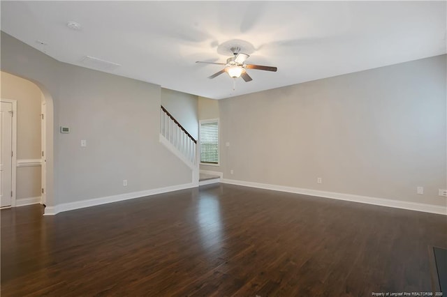 unfurnished room with arched walkways, ceiling fan, baseboards, stairs, and dark wood finished floors