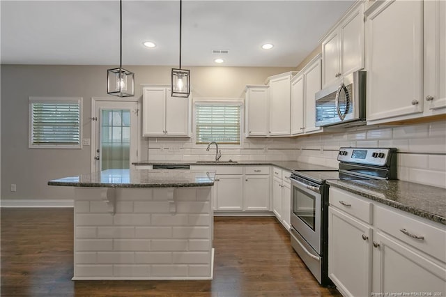 kitchen with appliances with stainless steel finishes, a kitchen island, a sink, and white cabinetry