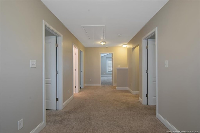 corridor featuring light carpet, attic access, and baseboards