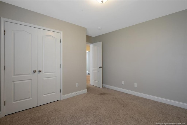 unfurnished bedroom featuring light carpet, a closet, and baseboards