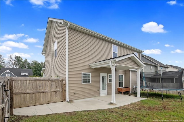 back of property featuring a patio area, a trampoline, fence, and a yard