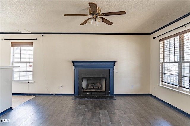 unfurnished living room with ceiling fan, a textured ceiling, wood finished floors, a fireplace with flush hearth, and ornamental molding