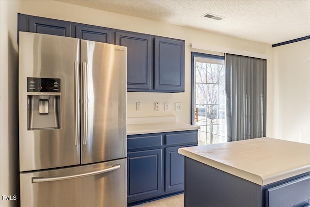 kitchen featuring a textured ceiling, blue cabinets, visible vents, light countertops, and stainless steel fridge