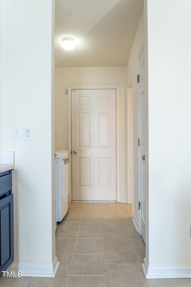 hallway featuring baseboards, a textured ceiling, and washing machine and clothes dryer