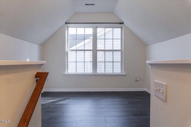 bonus room featuring dark wood-type flooring, lofted ceiling, visible vents, and a textured ceiling