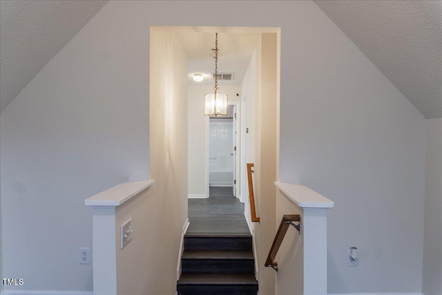 staircase featuring lofted ceiling, a textured ceiling, wood finished floors, visible vents, and baseboards