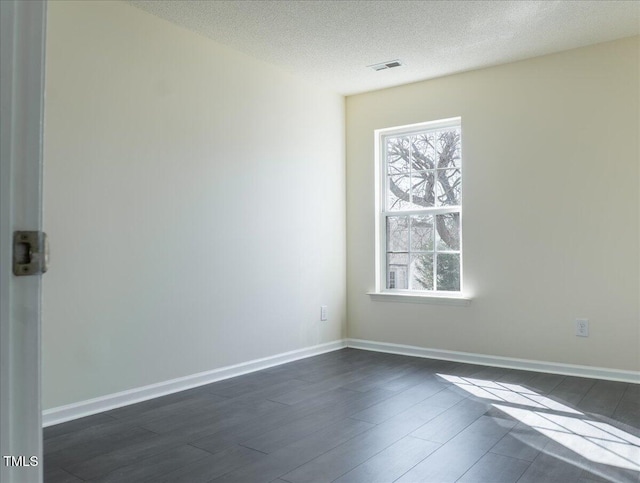 unfurnished room featuring visible vents, dark wood finished floors, a textured ceiling, and baseboards