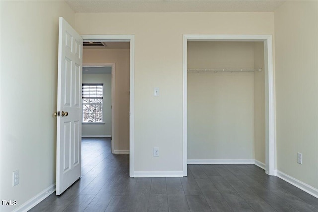 unfurnished bedroom with a closet, dark wood finished floors, visible vents, and baseboards