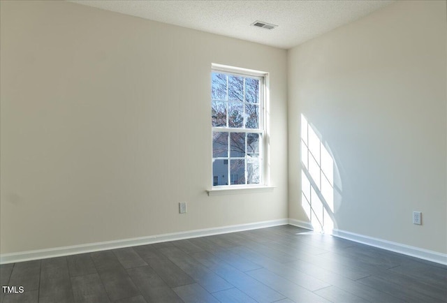 empty room featuring a textured ceiling, dark wood-type flooring, visible vents, and baseboards