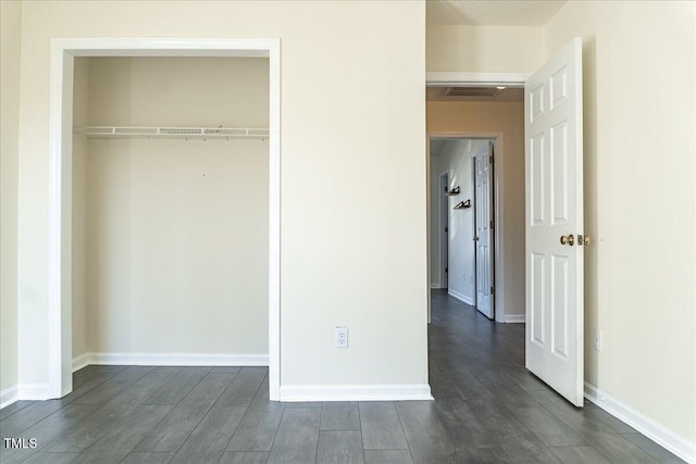 unfurnished bedroom featuring a closet, dark wood finished floors, visible vents, and baseboards