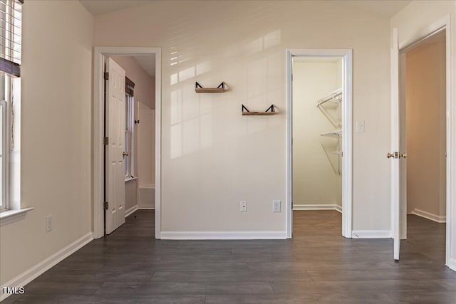 interior space featuring dark wood-style flooring, a walk in closet, and baseboards