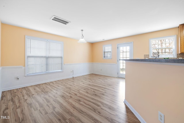 unfurnished living room featuring a wainscoted wall, wood finished floors, visible vents, and baseboards