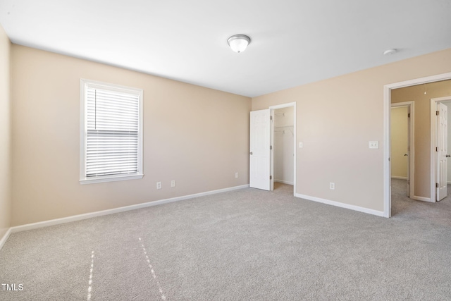 unfurnished bedroom with carpet floors, a walk in closet, and baseboards