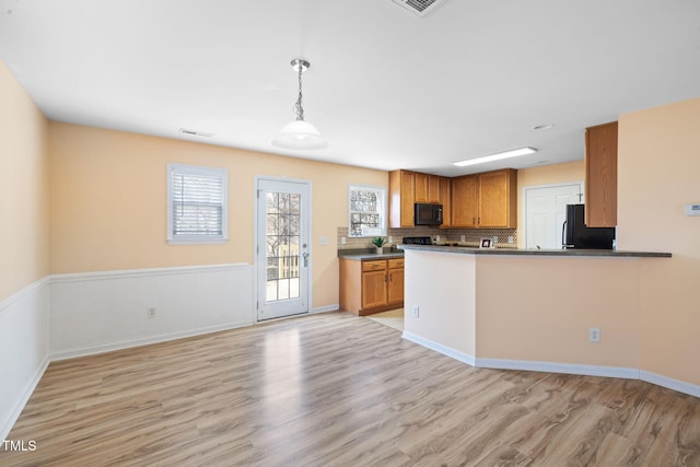 kitchen with light wood finished floors, decorative backsplash, brown cabinetry, dark countertops, and black appliances