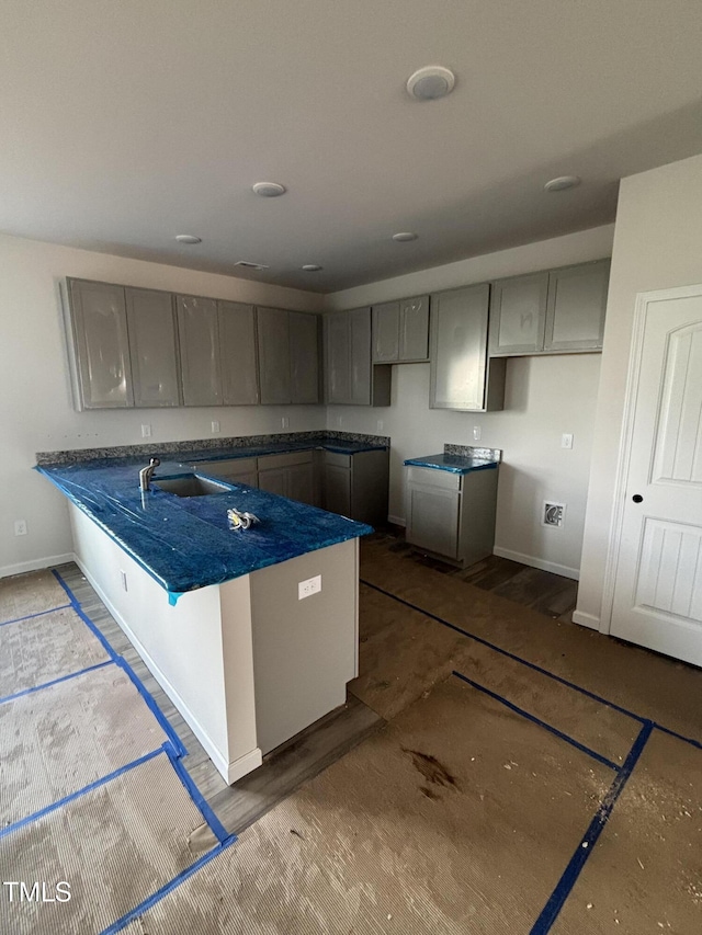 kitchen featuring gray cabinets, baseboards, a peninsula, and a sink