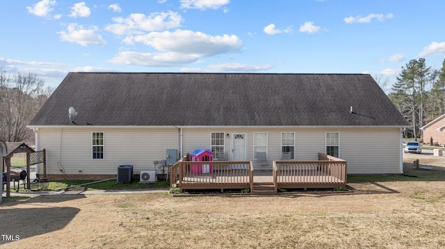 rear view of house featuring central AC unit, a wooden deck, a lawn, and a shingled roof