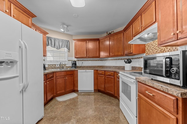 kitchen featuring tasteful backsplash, under cabinet range hood, brown cabinetry, white appliances, and a sink