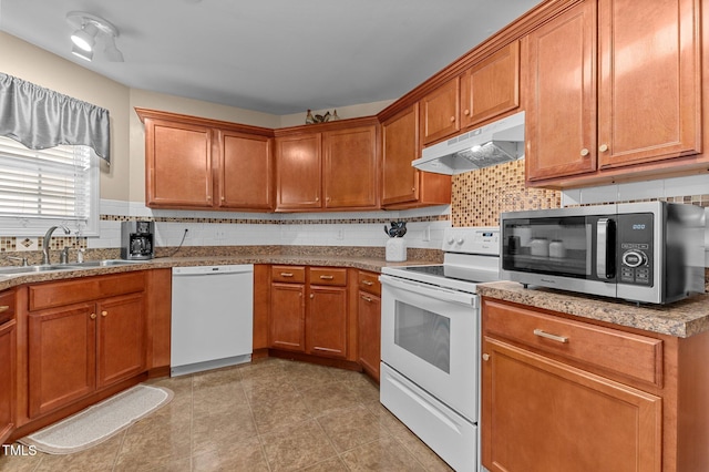 kitchen with under cabinet range hood, a sink, tasteful backsplash, white appliances, and brown cabinetry