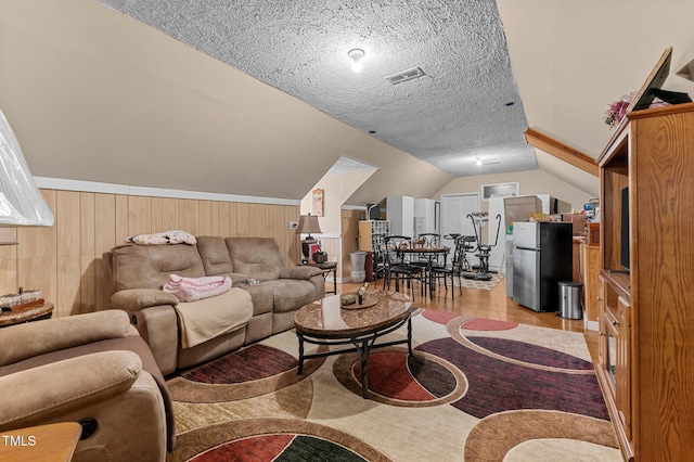 living room with a wainscoted wall, visible vents, vaulted ceiling, a textured ceiling, and light wood-type flooring