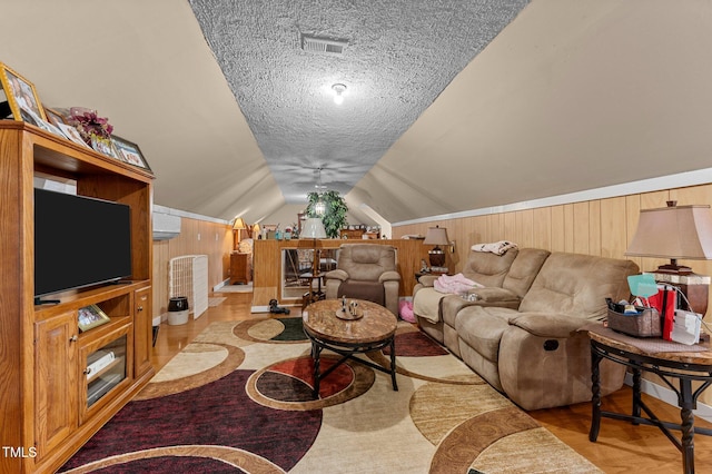 living room with visible vents, a textured ceiling, wood finished floors, wood walls, and vaulted ceiling