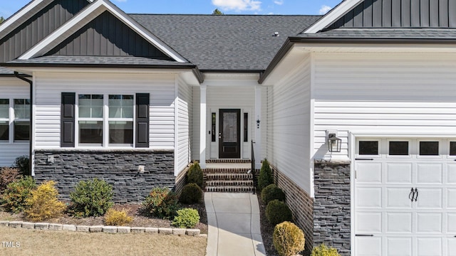 view of exterior entry featuring a garage, stone siding, a shingled roof, and board and batten siding