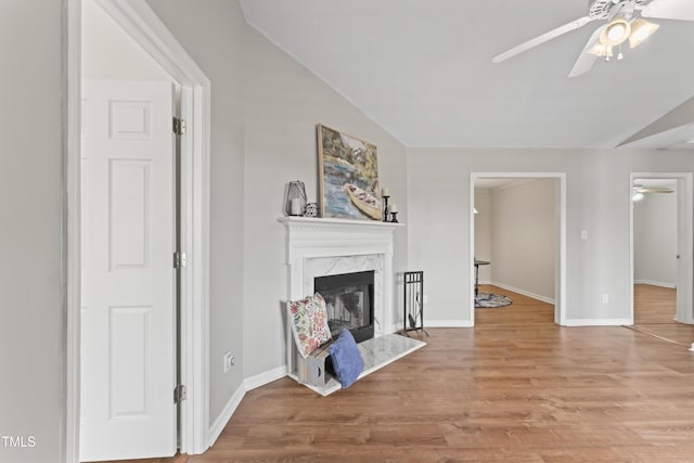 living area with ceiling fan, a premium fireplace, wood finished floors, baseboards, and vaulted ceiling