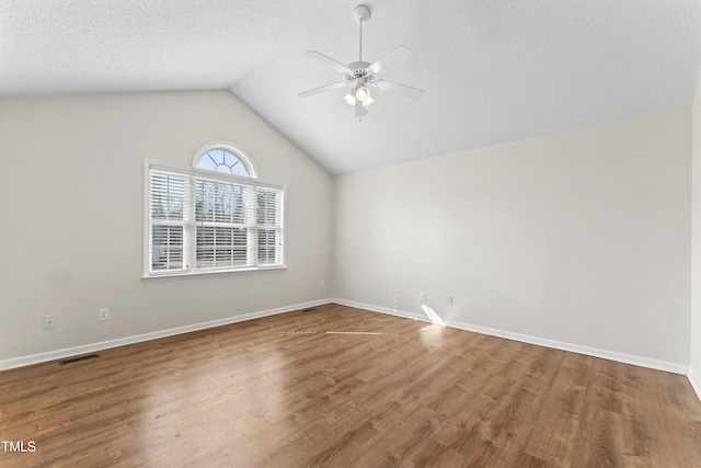 empty room with lofted ceiling, visible vents, a textured ceiling, wood finished floors, and baseboards