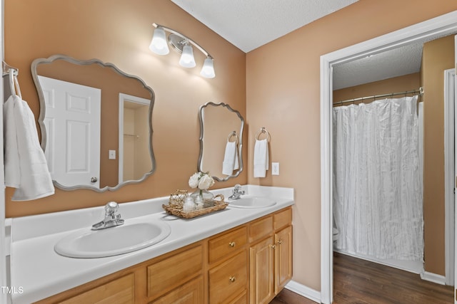 full bath with a textured ceiling, double vanity, wood finished floors, and a sink