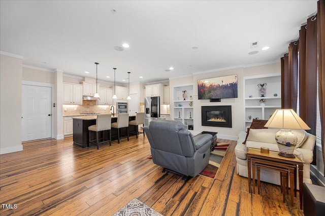 living area with a glass covered fireplace, recessed lighting, wood finished floors, and crown molding